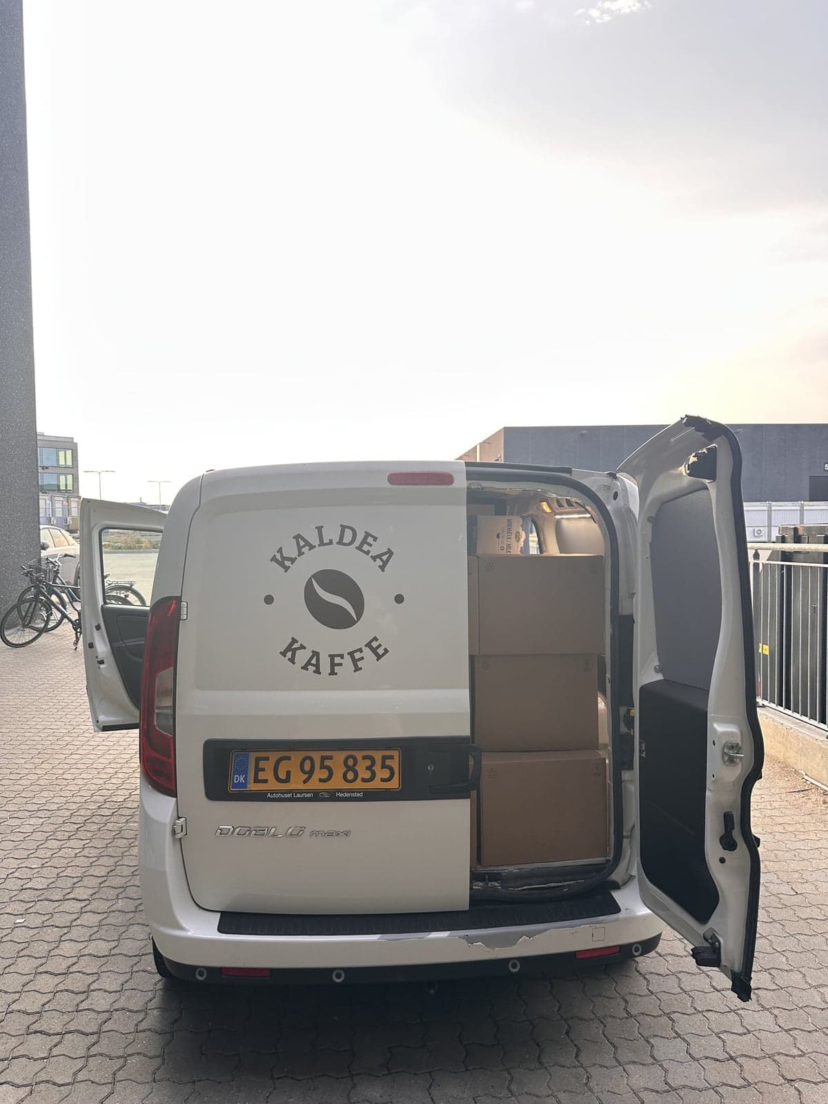 Kaldeas hvide varevogn med Kaldea Kaffe-logoet på bagdøren, den ene dør åben og kasser stablet i lastrummet